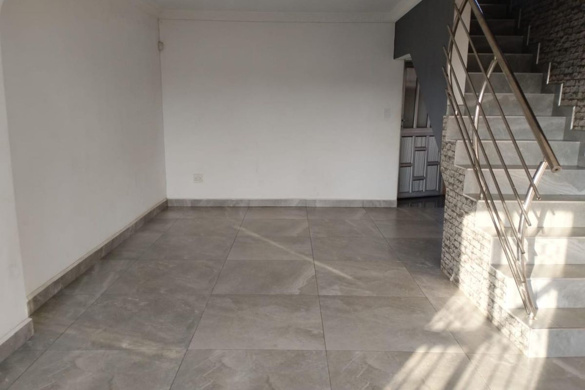 An empty, open-plan living area featuring modern large-format floor tiles, a stone-clad staircase with a stainless steel balustrade, and neutral wall finishes.