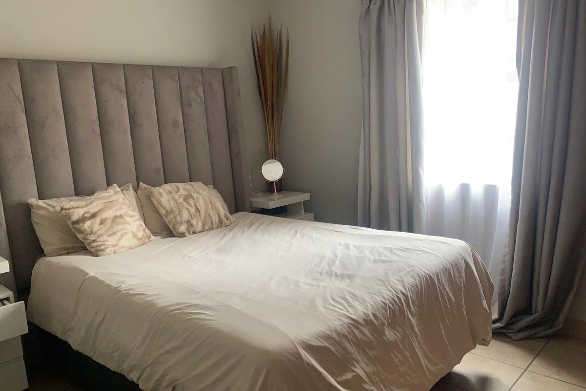 A well-maintained bedroom featuring neutral wall tones, tiled flooring, and a large window with installed curtain tracks.