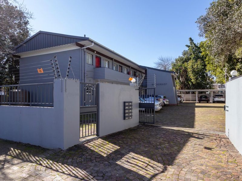 Exterior view of the apartment complex featuring a paved driveway, secure perimeter wall with electric fencing, and covered parking bays.