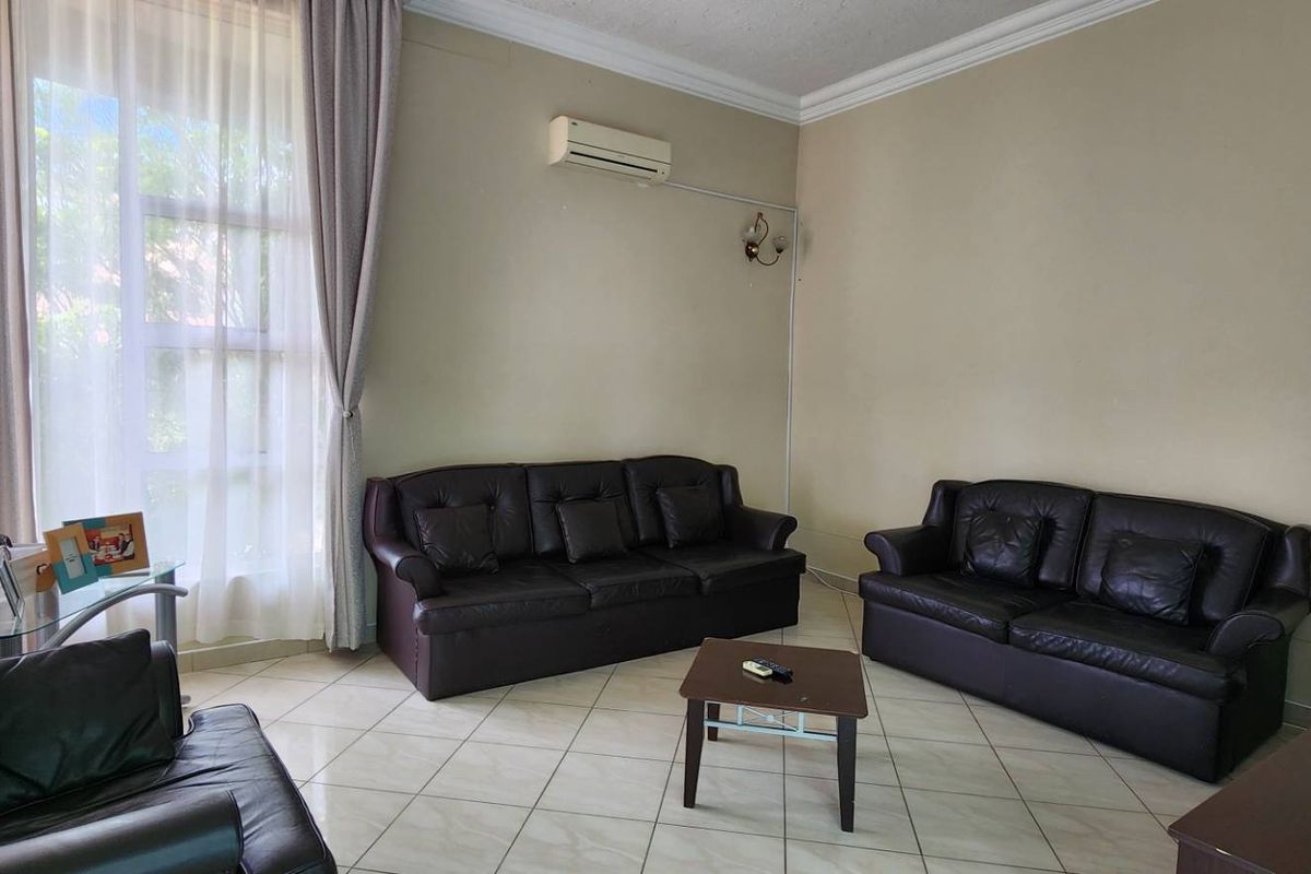 A living room featuring tiled flooring, crown molding, and a wall-mounted air conditioning unit, with large windows providing natural light.