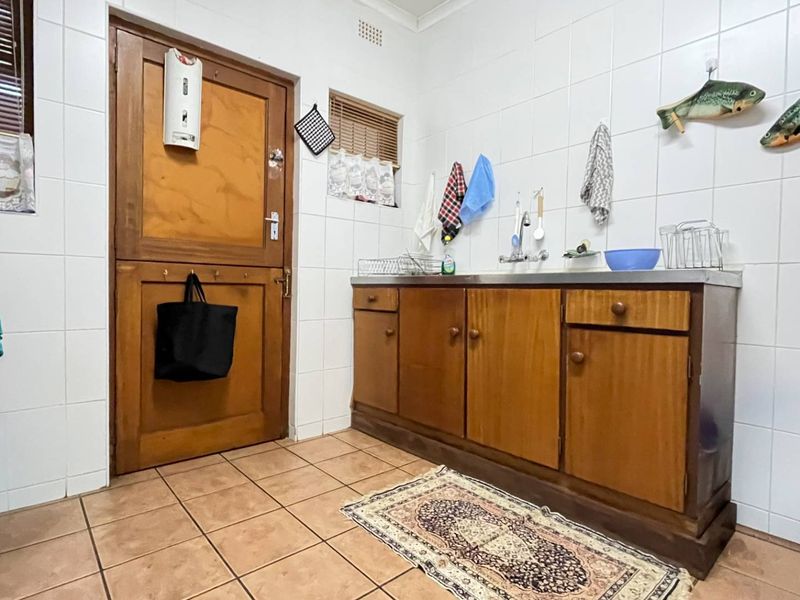 A functional laundry area featuring tiled walls, tiled flooring, built-in wooden cabinetry with a stainless steel sink, and a traditional stable door.