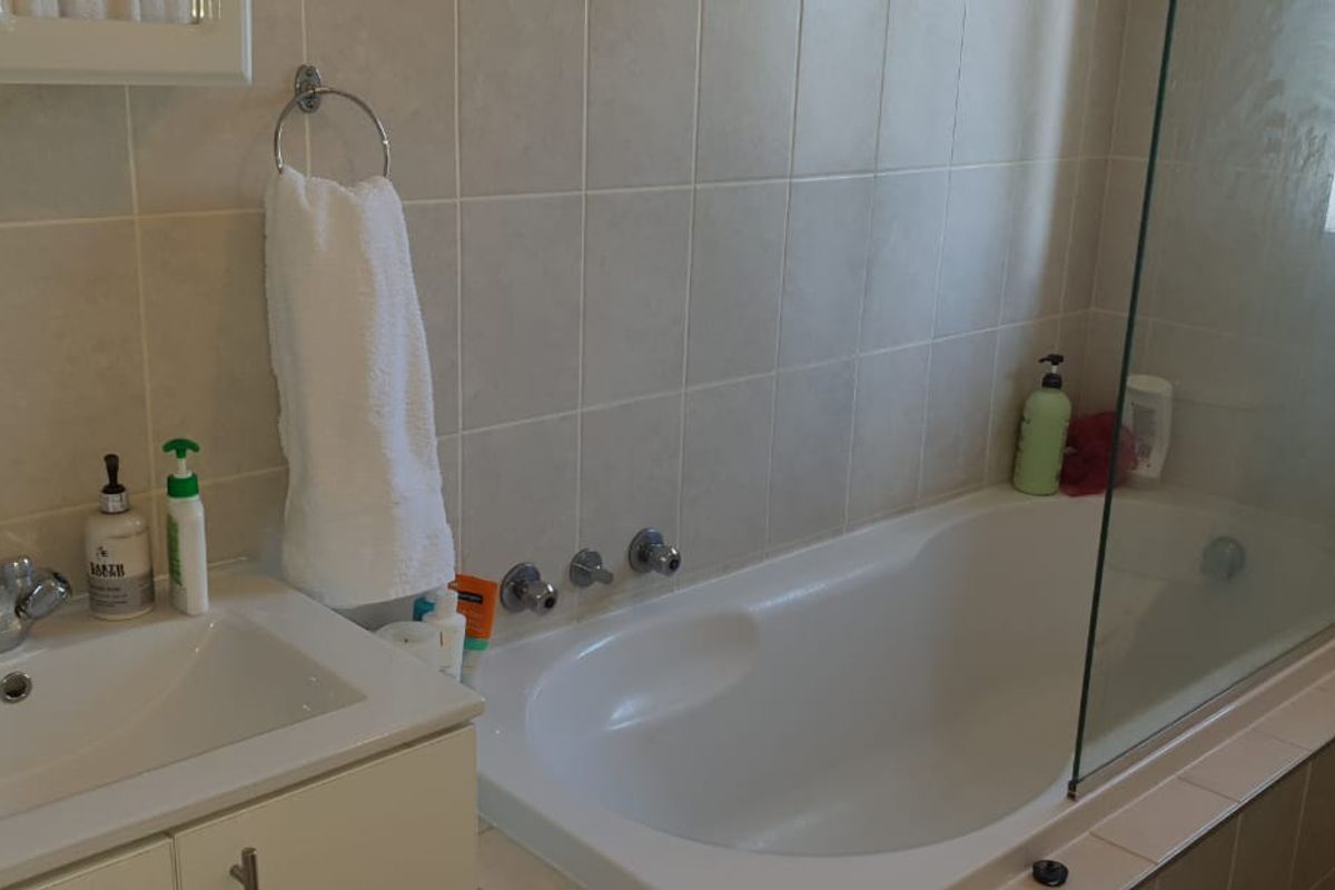 A functional bathroom featuring a built-in vanity with basin, a bathtub with a glass shower screen, and neutral wall tiling.