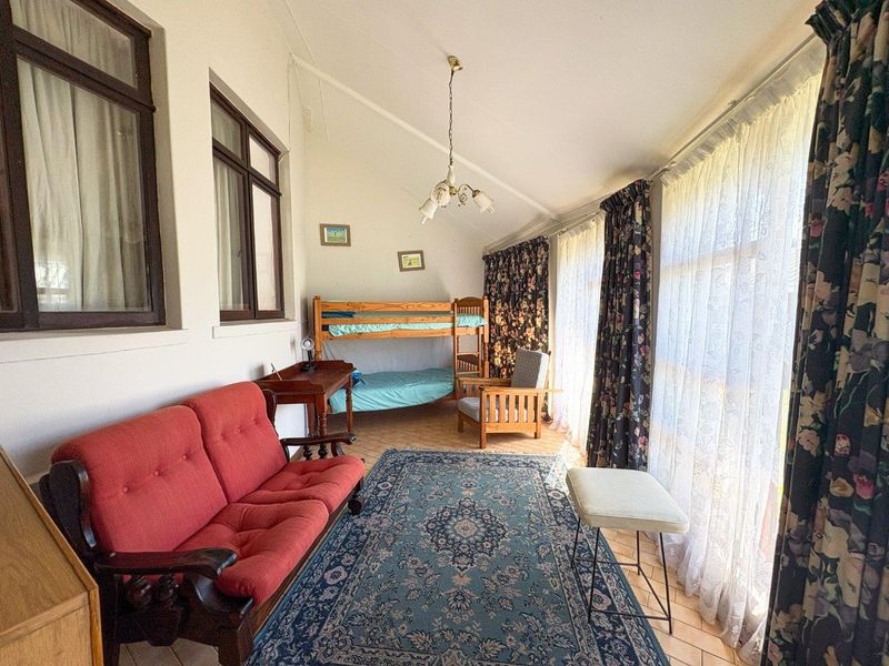 A spacious bedroom featuring tiled flooring, a vaulted ceiling, and large windows that provide ample natural light.