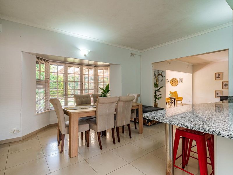 Open plan dining and kitchen area featuring tiled flooring, a granite breakfast bar, and a large bay window overlooking the garden.