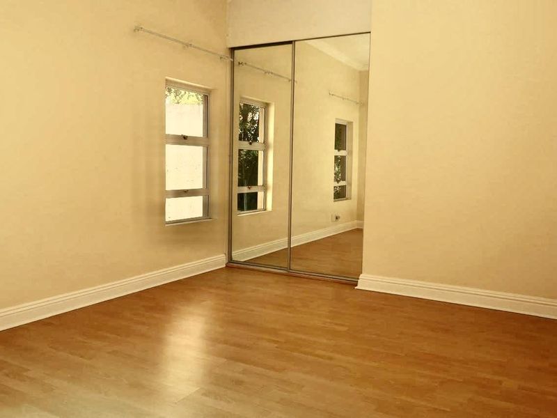 An empty bedroom featuring laminate flooring, mirrored sliding wardrobe doors, and casement windows with neutral wall finishes.