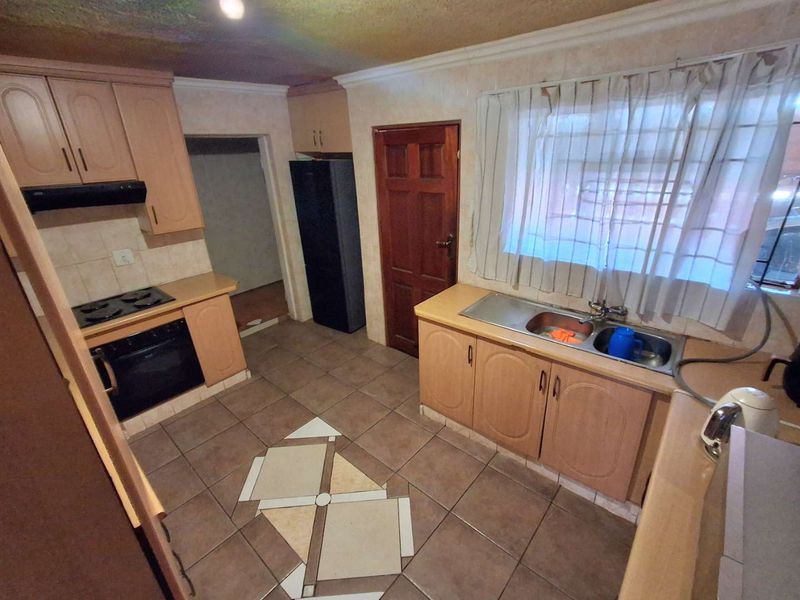 A functional kitchen featuring built-in cabinetry, a double bowl sink, and integrated cooking appliances, with tiled flooring and backsplash throughout.