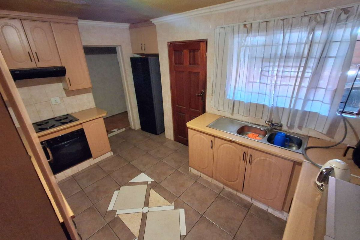 A functional kitchen featuring built-in cabinetry, a double bowl sink, and integrated cooking appliances, with tiled flooring and backsplash throughout.
