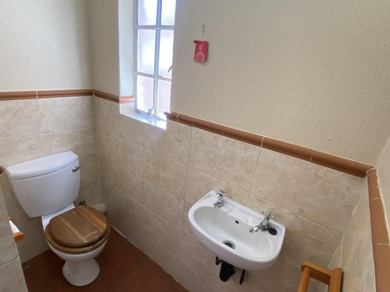 A compact guest bathroom featuring neutral wall tiling, terracotta flooring, a wall-mounted basin, and a close-coupled toilet.