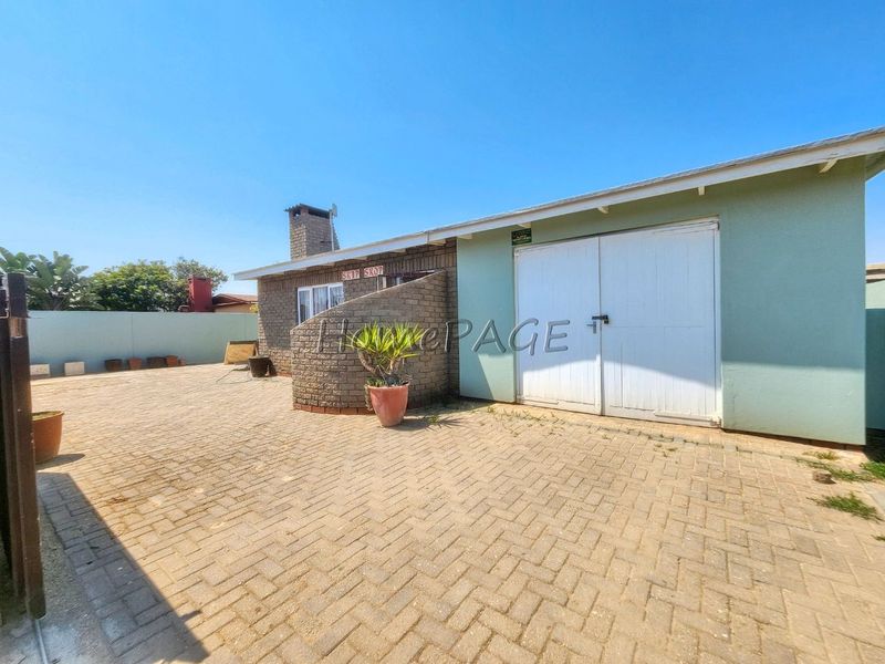 Rear exterior view featuring a paved courtyard, brick chimney, and double garage doors with a surrounding boundary wall.