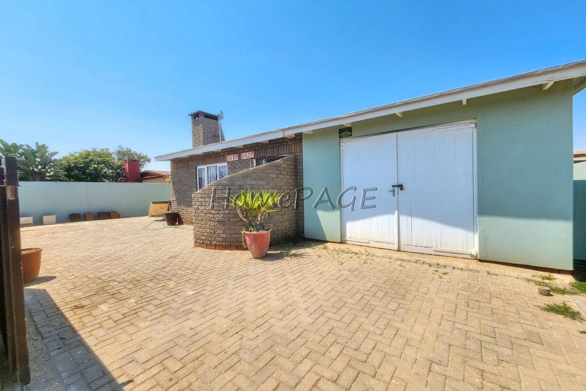 Rear exterior view featuring a paved courtyard, brick chimney, and double garage doors with a surrounding boundary wall.