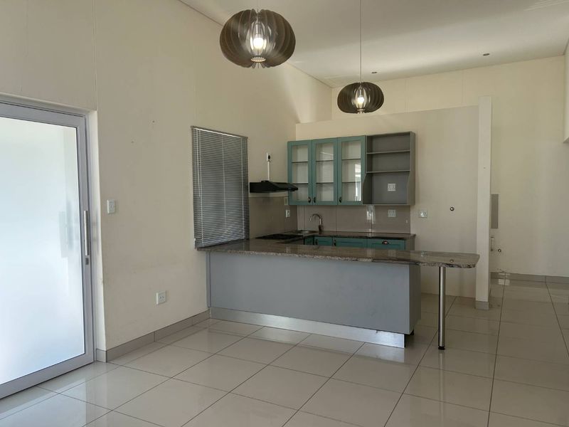 Open plan kitchen area featuring granite countertops, built-in cabinetry, and tiled flooring, leading out through a glass sliding door.