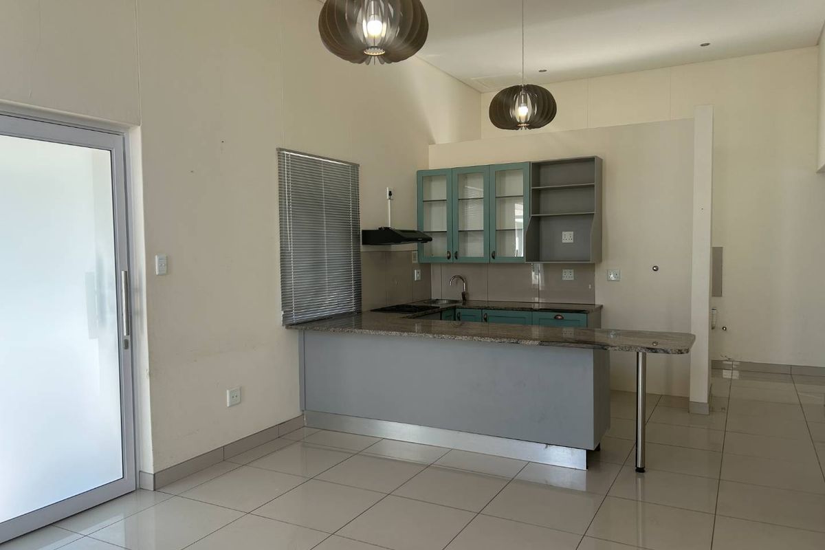 Open plan kitchen area featuring granite countertops, built-in cabinetry, and tiled flooring, leading out through a glass sliding door.