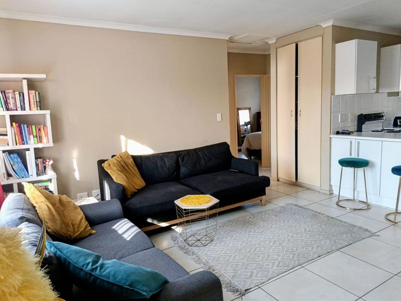 Open-plan living area featuring tiled floors, built-in storage cupboards, and a compact kitchen space with modern cabinetry and integrated appliances.