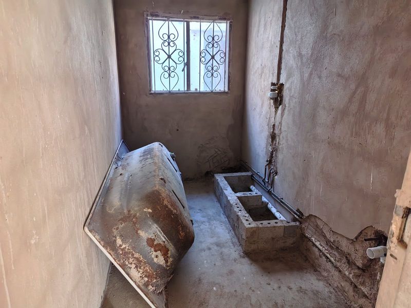 A bathroom in a state of renovation, featuring exposed plumbing, unfinished plaster walls, and a masonry vanity base ready for new fixtures.