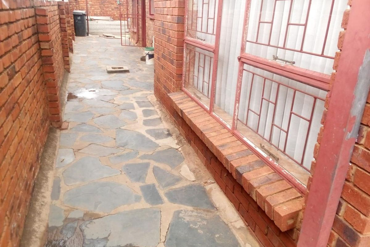 A narrow exterior side passage featuring stone paving, face brick walls, and metal security bars on the windows.