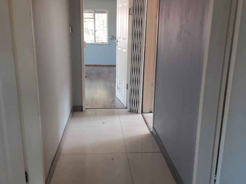 A functional hallway featuring tiled flooring and access to adjacent rooms, including a security gate and internal doors.