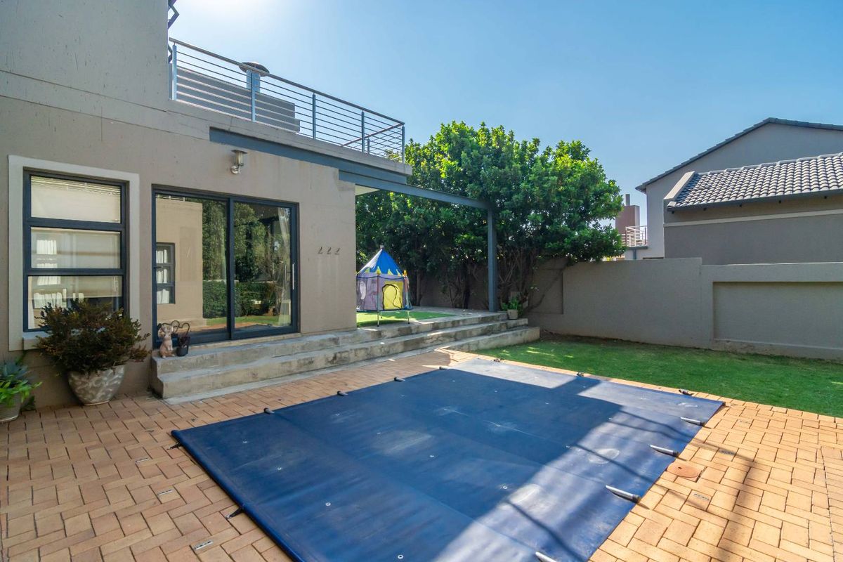 Rear exterior view featuring a paved patio area, a swimming pool with a safety cover, and an upper-level balcony with metal railings.