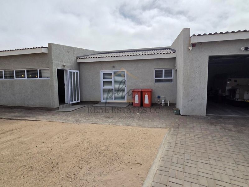 Rear exterior view of the property featuring a paved patio area, access to the garage, and multiple window and door entry points.