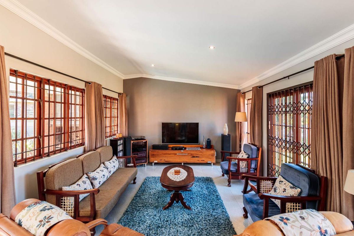 A well-maintained living room featuring tiled flooring, recessed downlighting, decorative cornice, and secure metal security gates on the windows and doors.