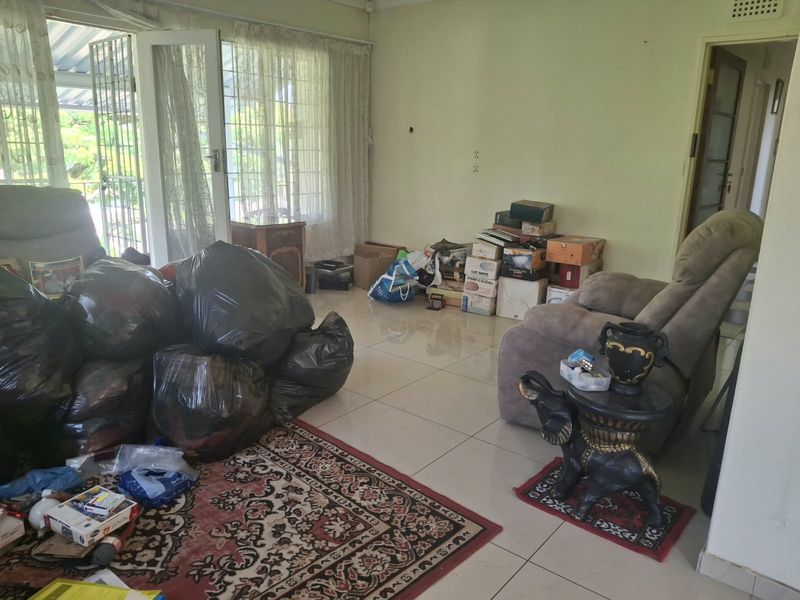 A living room featuring tiled flooring and glass sliding doors leading to an outdoor area, currently requiring cosmetic updates and decluttering.