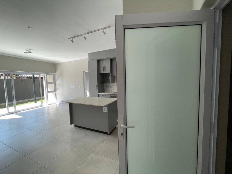 Modern open-plan living area featuring a kitchen island, neutral tiled flooring, and large sliding glass doors leading to an outdoor space.