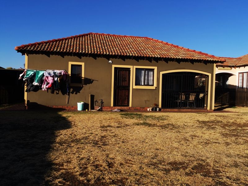 Rear view of the house featuring a covered patio, terracotta tiled roof, and secure window and door fittings overlooking a private garden area.