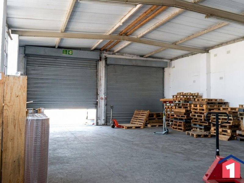 Spacious industrial warehouse unit featuring high ceilings with exposed steel trusses, concrete flooring, and dual roller shutter doors for efficient access.