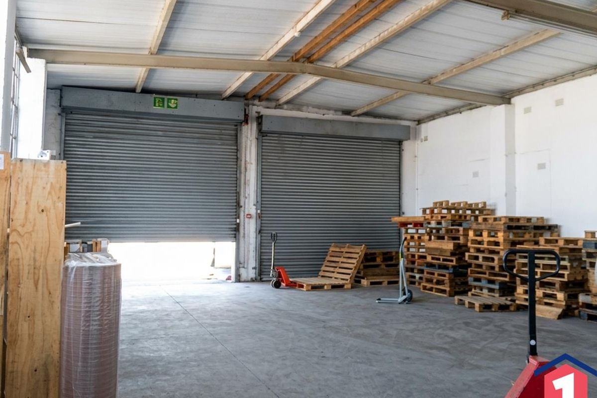 Spacious industrial warehouse unit featuring high ceilings with exposed steel trusses, concrete flooring, and dual roller shutter doors for efficient access.