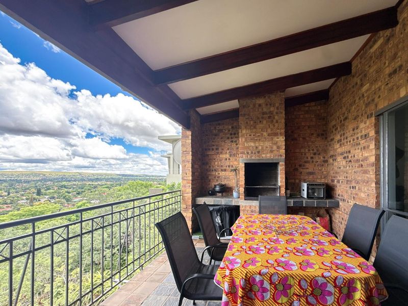 Covered balcony featuring a built-in brick braai, exposed timber ceiling beams, and expansive elevated views over the surrounding landscape.
