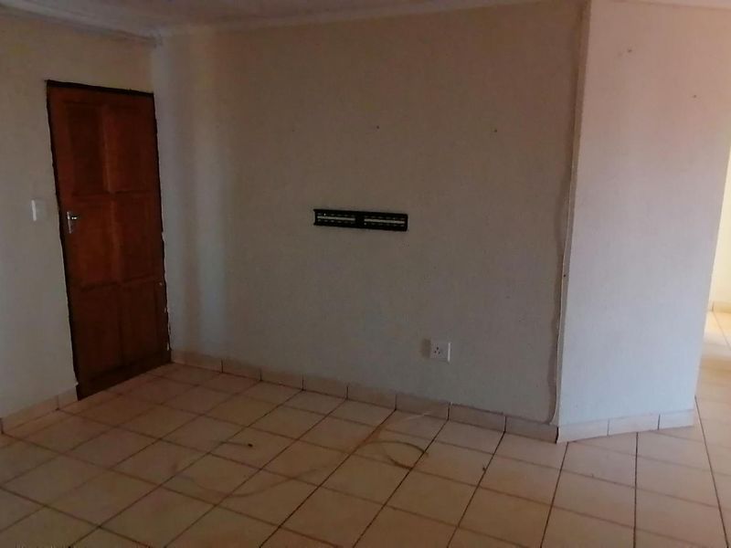 An empty living area featuring tiled flooring, a wall-mounted television bracket, and a timber door, requiring minor cosmetic updates.