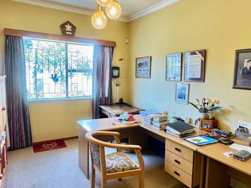 A functional home office space featuring a built-in desk, carpeted flooring, and a window fitted with security bars.
