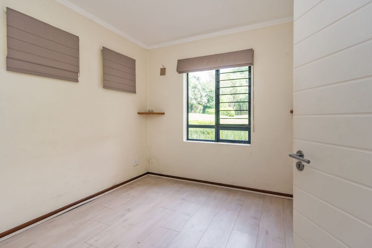 A bright, empty bedroom featuring light-toned laminate flooring, neutral walls, and a window with fitted blinds overlooking the garden.