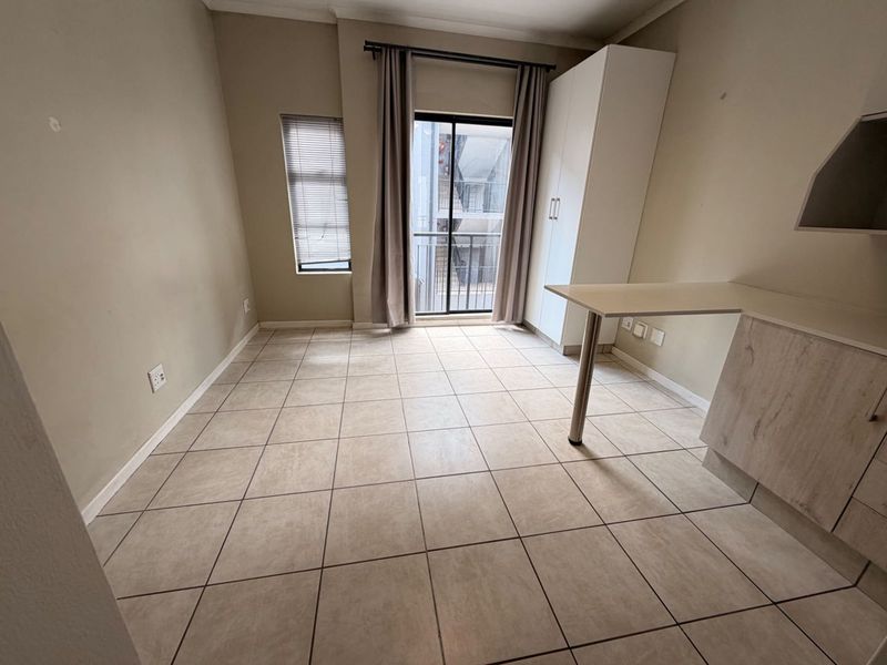 An open-plan living area featuring tiled flooring, a built-in cupboard, a breakfast counter, and a sliding door leading to a balcony.