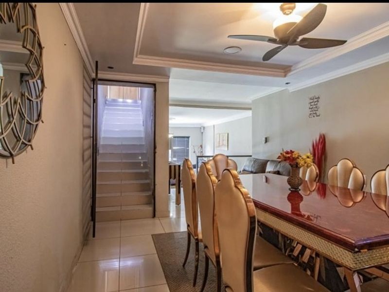 A well-lit dining area featuring tiled flooring, crown molding, and a ceiling fan, with an adjacent staircase leading to another level.