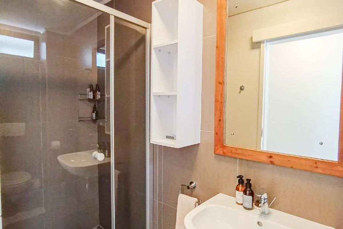 Modern bathroom featuring a wall-mounted basin, a glass-enclosed shower with pebble-style floor tiling, and a wooden-framed mirror.