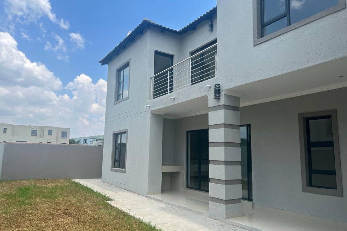 Rear view of a modern two-story house featuring a covered patio with a built-in braai, a balcony, and a private garden area.