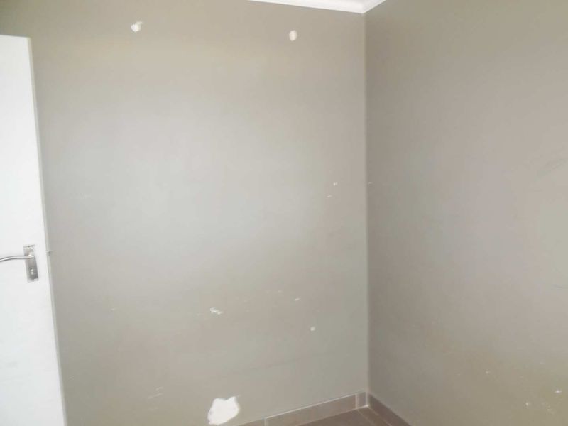 An empty room featuring tiled flooring and painted walls with visible surface imperfections requiring minor repairs and cosmetic attention.
