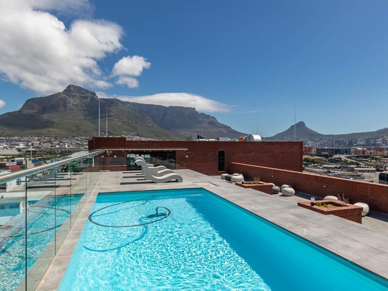Rooftop swimming pool area featuring a glass balustrade, tiled decking, and panoramic mountain views.