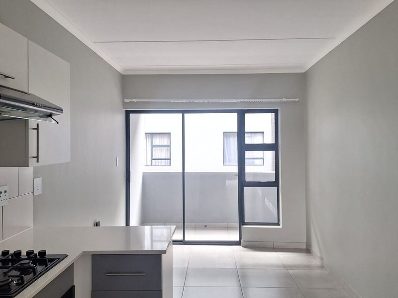 Modern open-plan kitchen and living area featuring tiled floors, built-in cabinetry with a gas hob, and access to a private balcony through sliding doors.