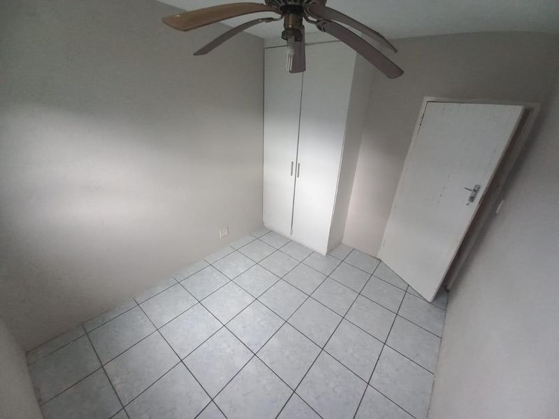 An empty bedroom featuring tiled flooring, a built-in wardrobe, and a ceiling fan, offering a blank canvas for personalization.