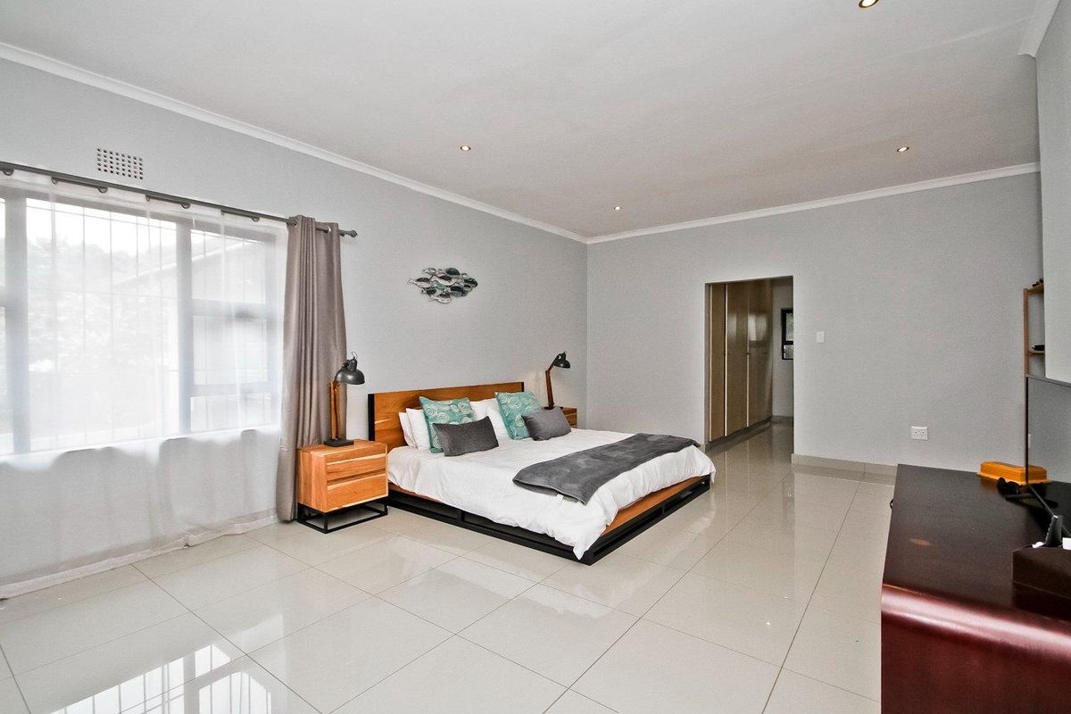 Spacious bedroom featuring polished porcelain floor tiles, recessed downlighting, and a neutral color palette with access to an adjoining walk-in closet area.