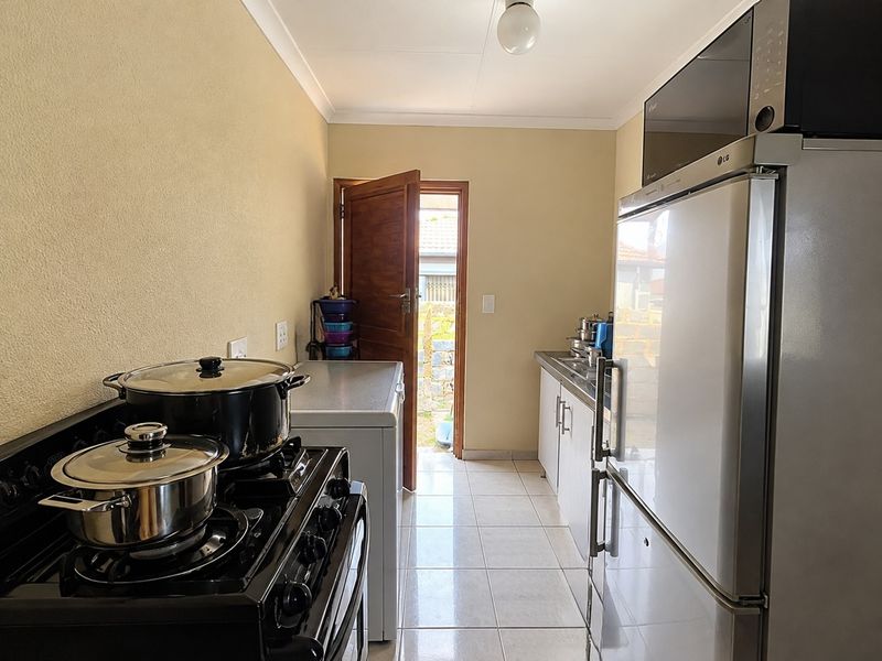 A functional scullery area featuring tiled flooring, built-in cabinetry, and a sink, with direct access to the exterior.