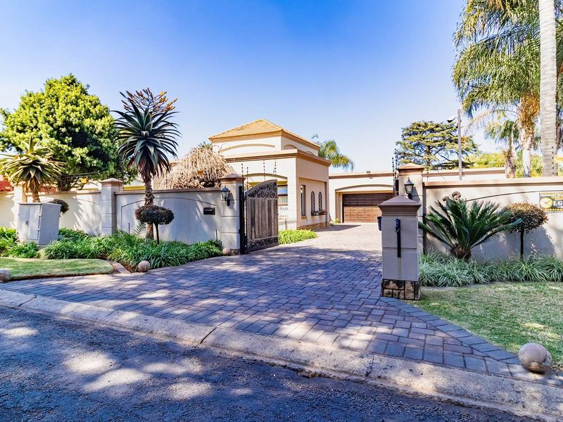 Front view of the property featuring a paved driveway, secure boundary wall with an electric gate, and a well-maintained landscaped garden.