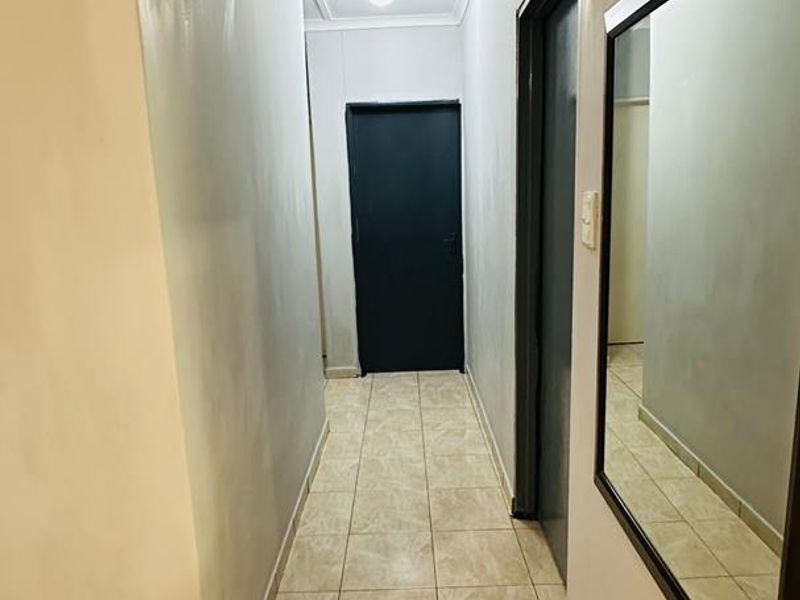 A clean, tiled hallway featuring neutral walls, cove cornicing, and access to multiple internal rooms.