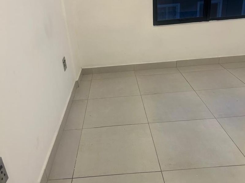 An empty bedroom featuring neutral tiled flooring, white walls, and a dark aluminium-framed window.