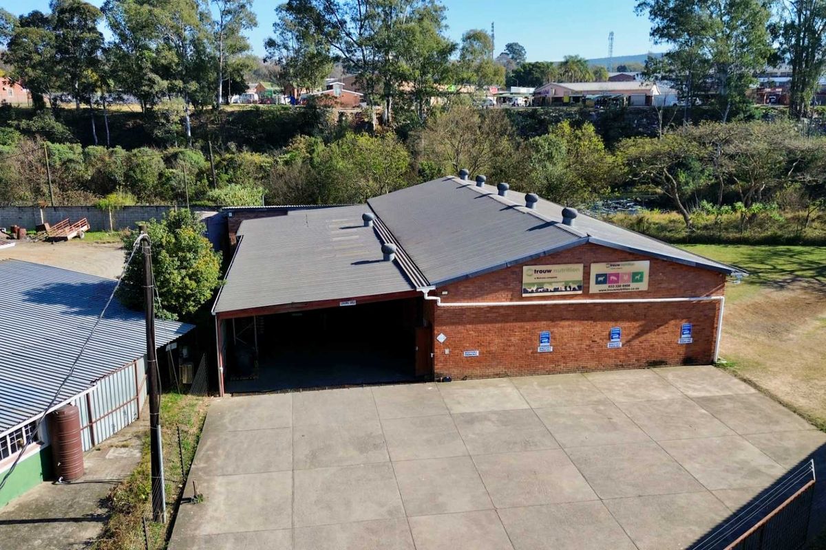 Aerial view of an industrial property featuring a brick warehouse building with a corrugated metal roof and a spacious concrete yard.
