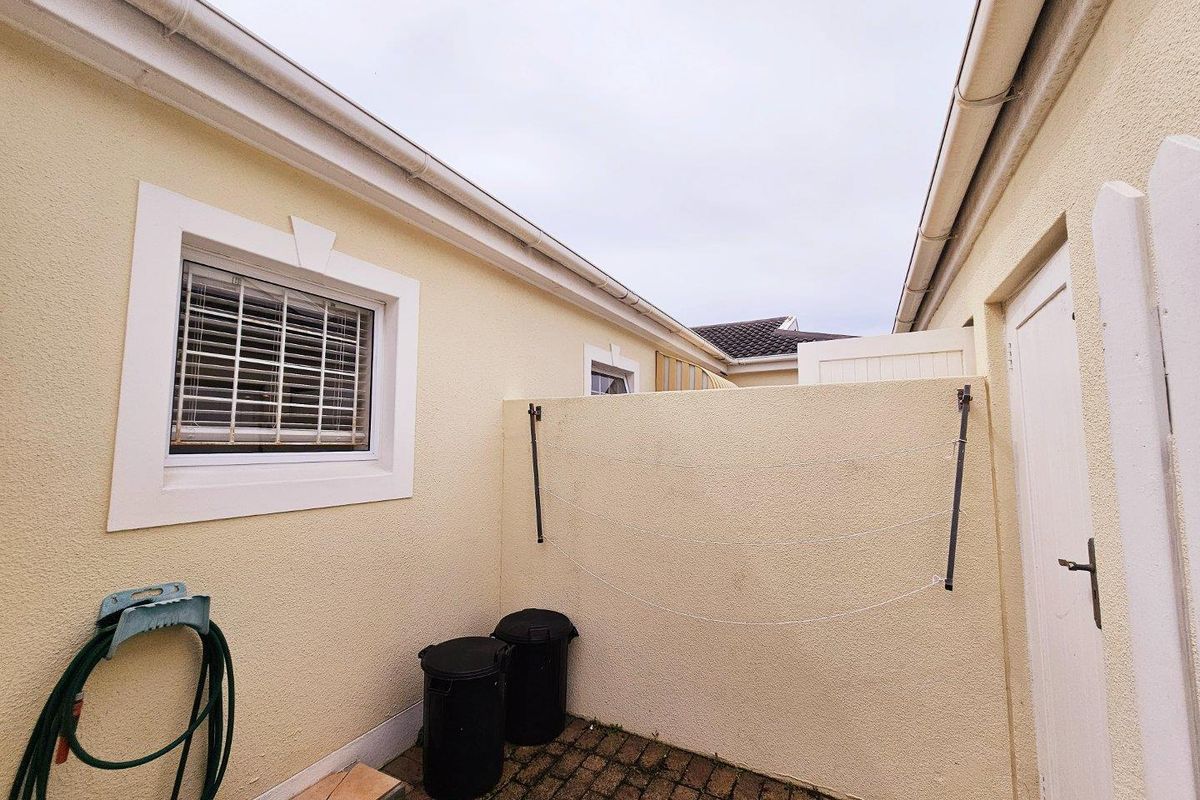 A paved rear courtyard area featuring a wall-mounted washing line, external access door, and guttering system.