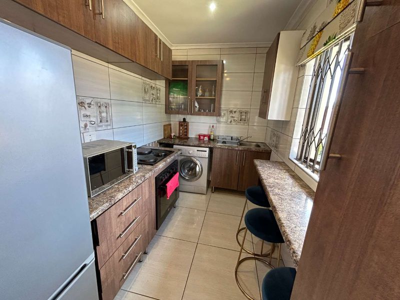 Compact kitchen featuring wood-finish cabinetry, laminate countertops, integrated oven and hob, tiled backsplash, and a breakfast bar area.
