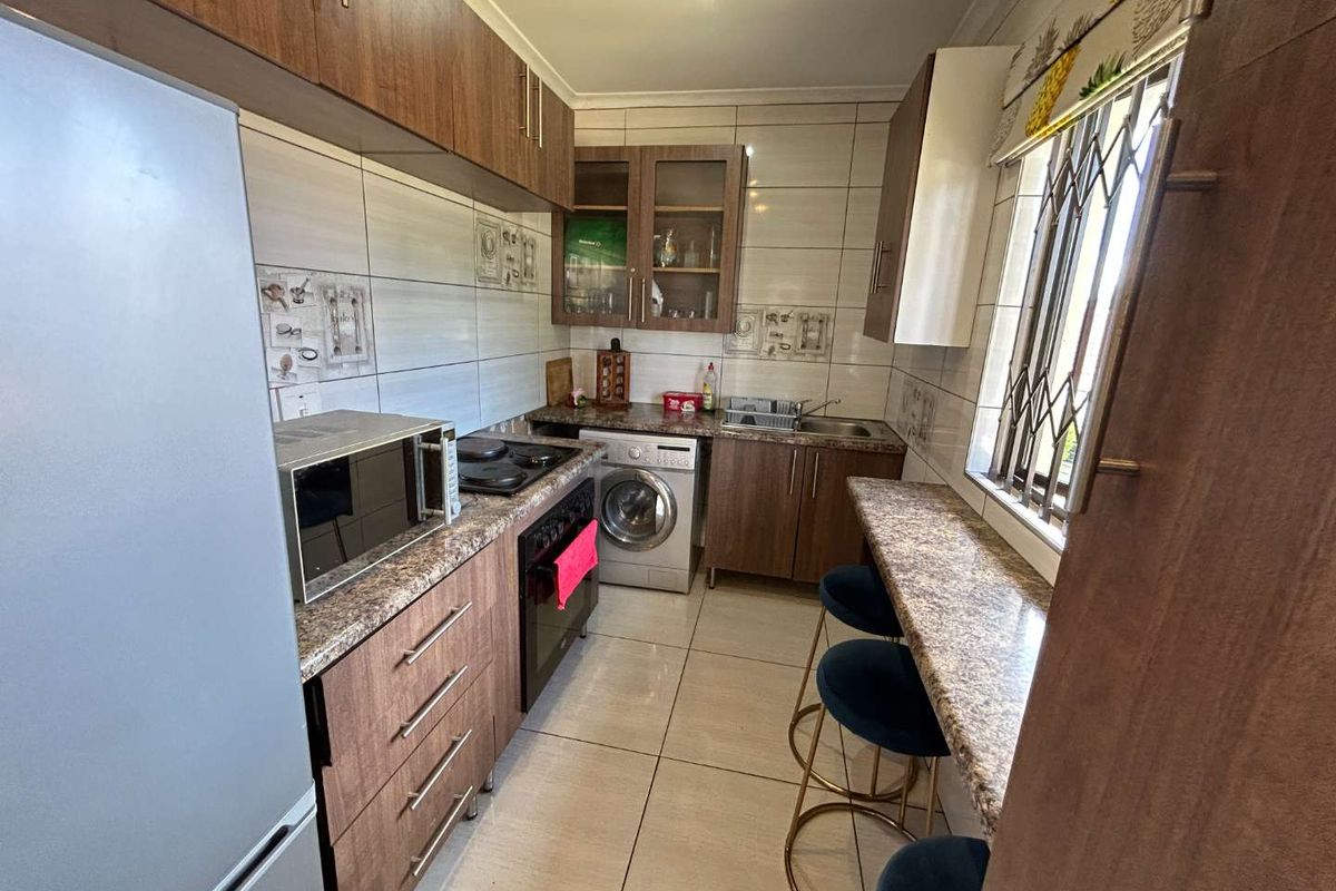 Compact kitchen featuring wood-finish cabinetry, laminate countertops, integrated oven and hob, tiled backsplash, and a breakfast bar area.