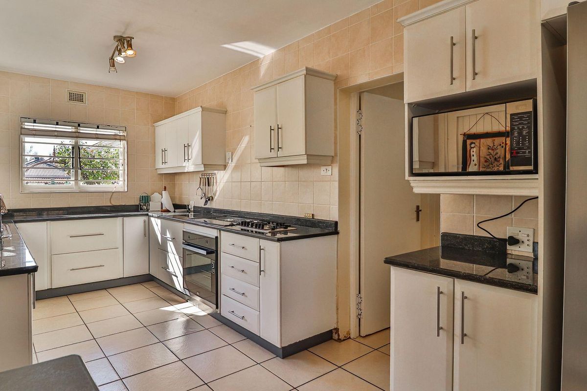 Functional kitchen featuring white cabinetry, dark granite countertops, built-in oven, gas hob, and tiled flooring with natural light.